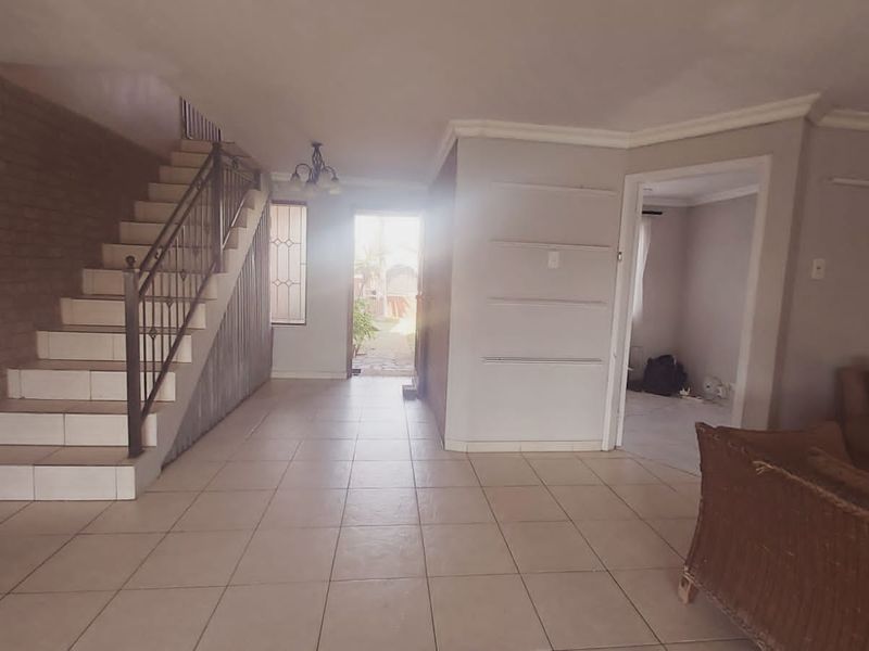 Open plan living area featuring tiled flooring, an exposed brick wall, and a staircase with a metal balustrade leading to the upper level.