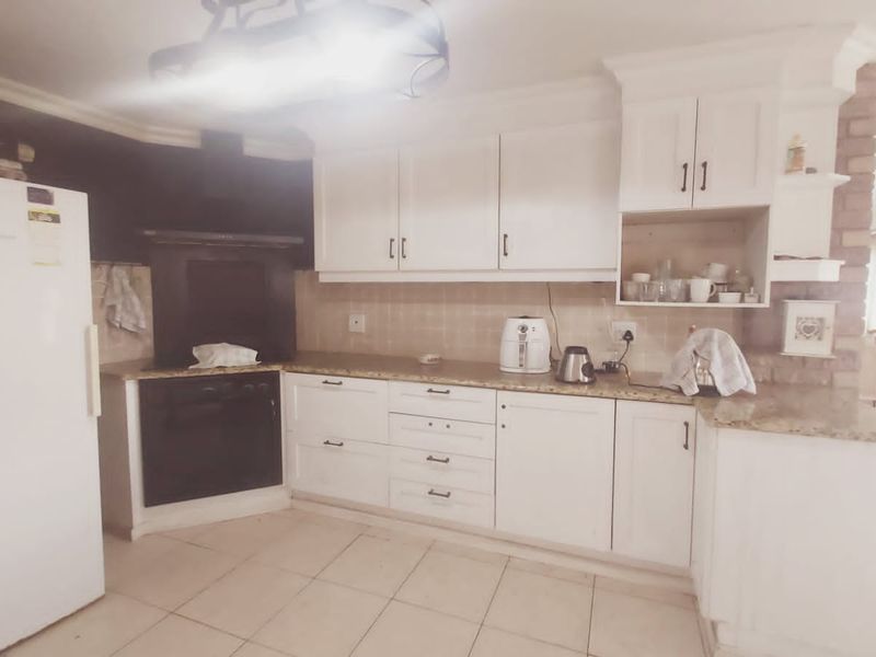 A functional kitchen featuring white cabinetry, granite countertops, built-in oven, extractor fan, and tiled flooring, with an adjacent exposed brick feature.