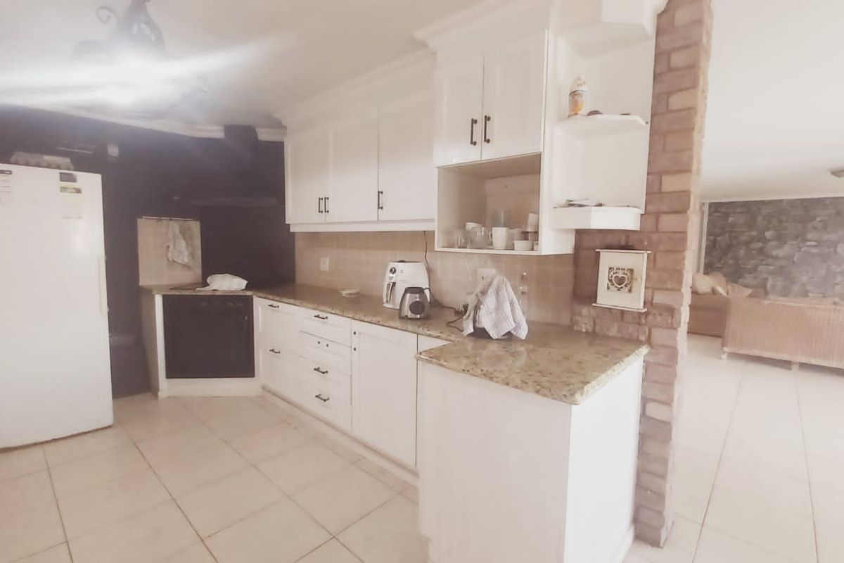 A functional kitchen featuring white cabinetry, granite countertops, built-in oven, and an exposed brick feature pillar, opening into an adjacent living area.