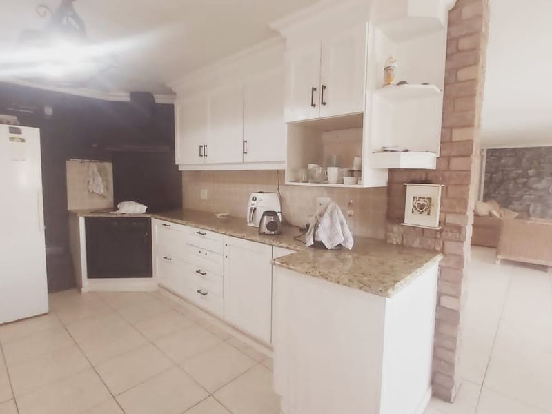 A functional kitchen featuring white cabinetry, granite countertops, built-in oven, and an exposed brick feature pillar, opening into an adjacent living area.