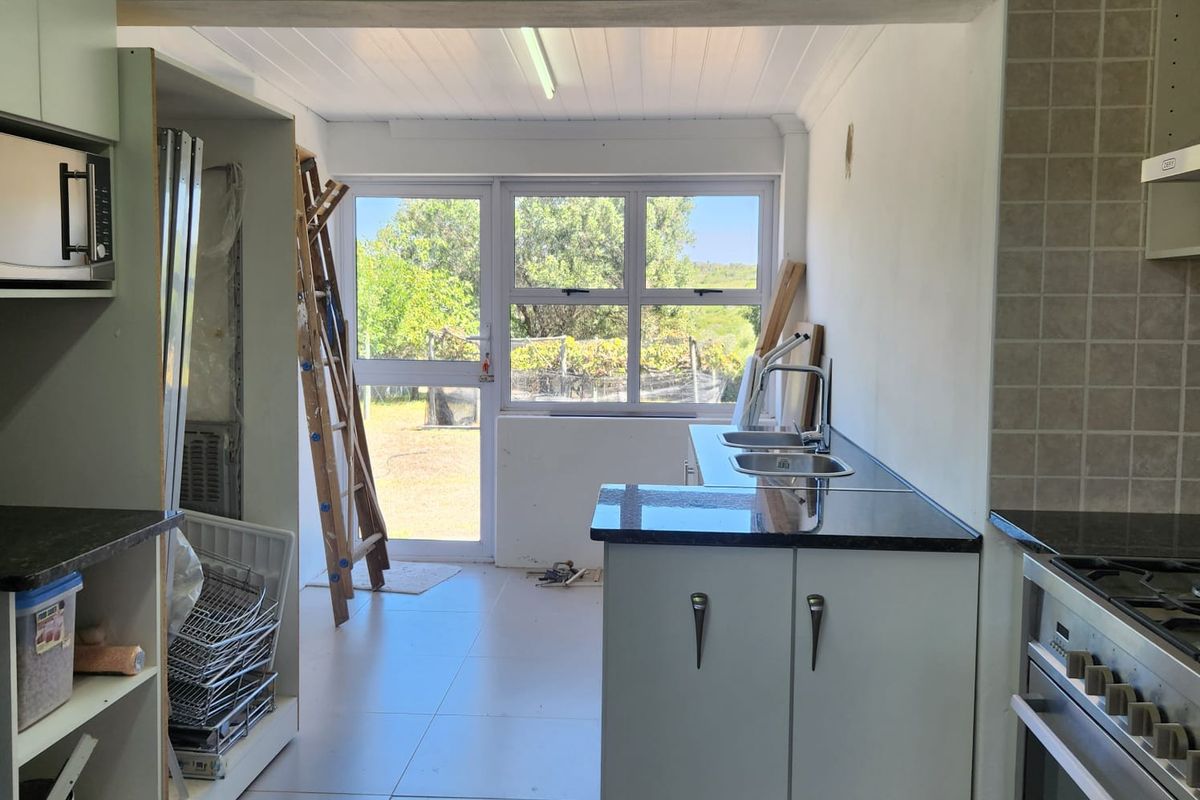 A functional kitchen space featuring granite countertops, a gas hob, and double sink, currently undergoing minor finishing work with direct garden access.