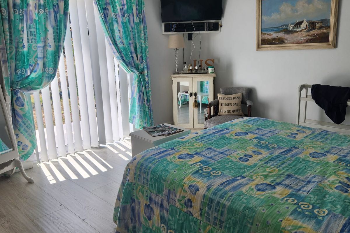 A bedroom featuring light-toned laminate flooring and a sliding glass door with vertical blinds, providing direct access to the exterior.