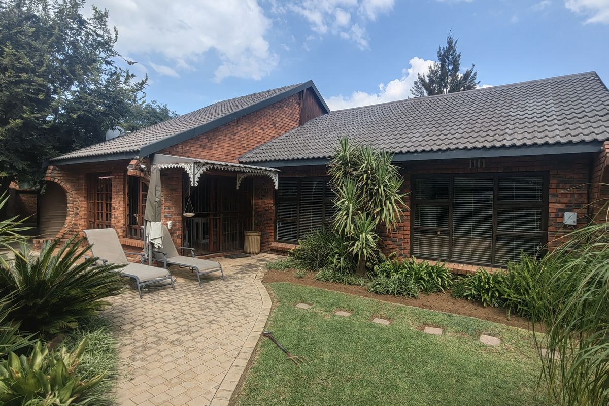 Rear view of a brick-faced house featuring a paved patio area, landscaped garden, and secure window treatments.