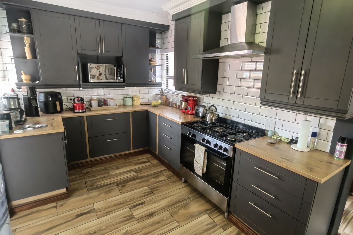 Modern kitchen featuring dark grey cabinetry, wooden countertops, subway tile backsplash, and stainless steel appliances, complemented by wood-look tile flooring.
