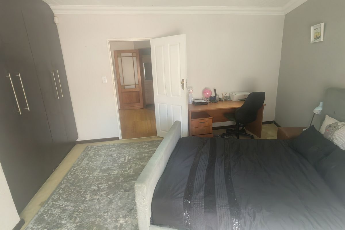 Spacious bedroom featuring dark built-in cupboards, recessed downlighting, and coved ceiling details, offering a functional layout with direct access to the hallway.