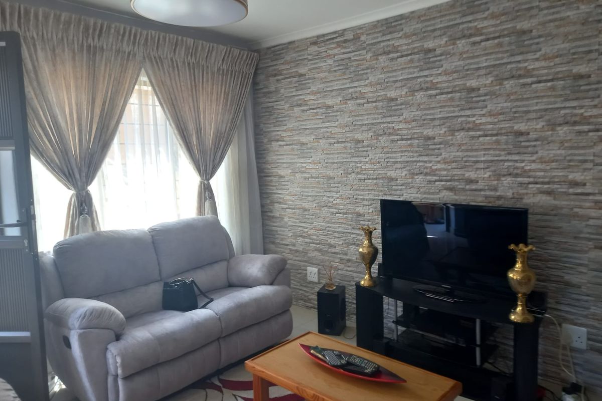 A cozy living room featuring a textured stone-cladding feature wall, large windows with curtains, and a central ceiling light fixture.