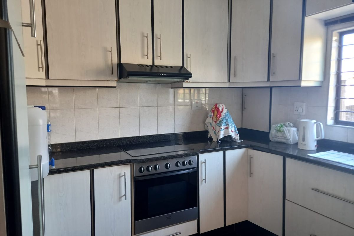 A functional kitchen featuring light-toned cabinetry, dark granite countertops, a built-in oven with extractor fan, and tiled splashbacks.