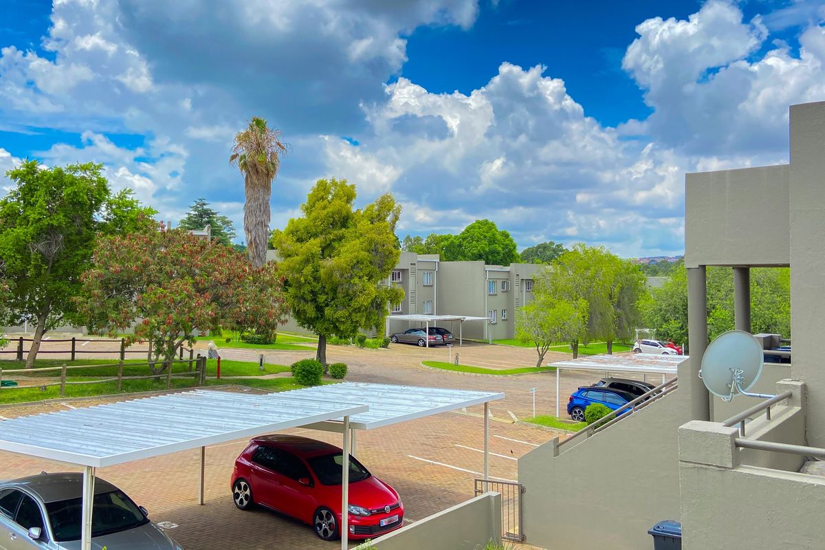 View of the apartment complex exterior, featuring paved parking areas with carports and landscaped grounds under a clear sky.