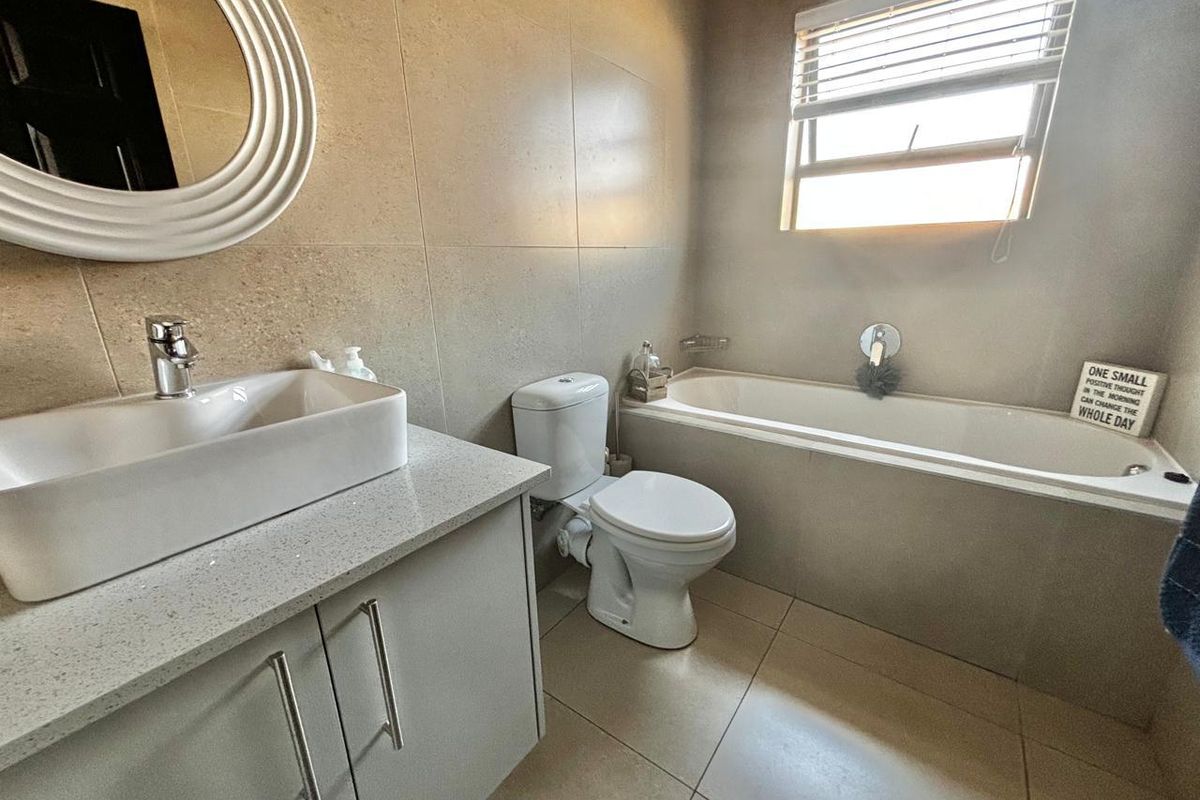 A modern bathroom featuring a vanity with a countertop basin, a toilet, and a built-in bathtub with neutral wall and floor tiling.