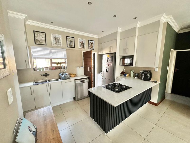 Modern kitchen featuring white cabinetry, stone countertops, a central island with a gas hob, and tiled flooring with recessed lighting.