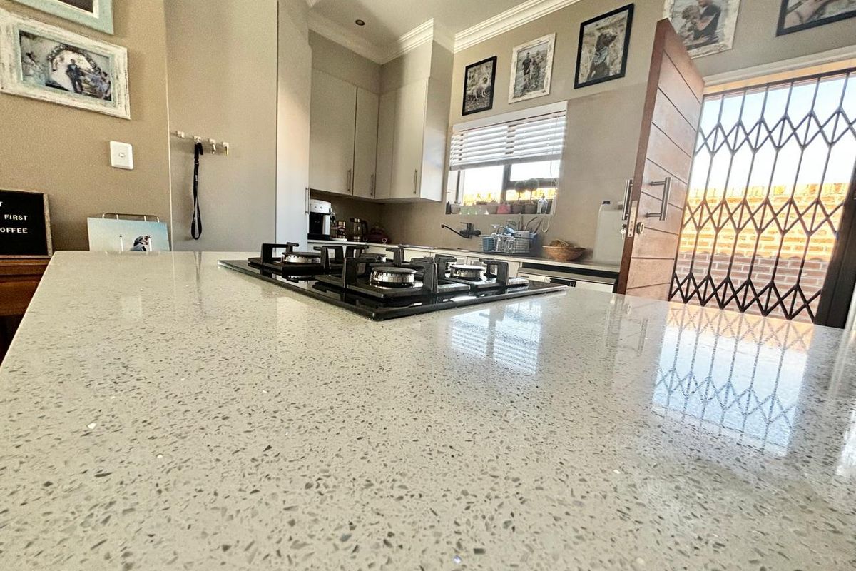 Modern kitchen featuring a spacious quartz island with an integrated gas hob, ample cabinetry, and direct access to an outdoor area via a security gate.