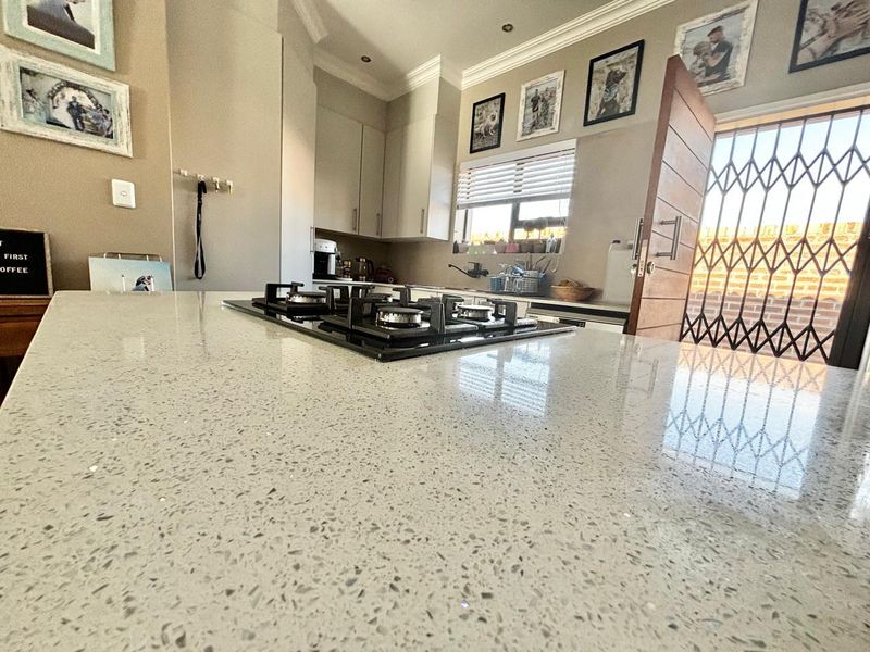 Modern kitchen featuring a spacious quartz island with an integrated gas hob, ample cabinetry, and direct access to an outdoor area via a security gate.