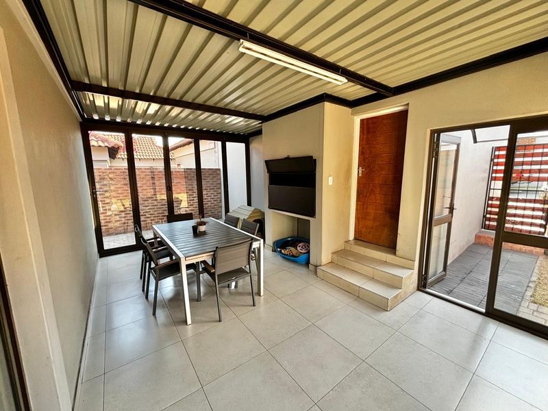 Covered patio area featuring tiled flooring, a built-in braai, and sliding glass doors providing access to the outdoor space.
