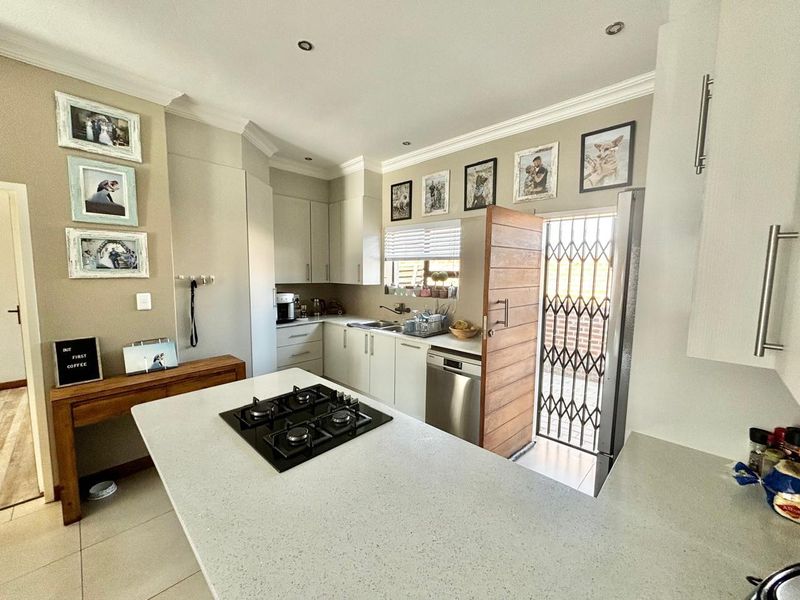 Modern kitchen featuring a central island with a gas hob, stone countertops, ample built-in cabinetry, and direct access to an outdoor area.