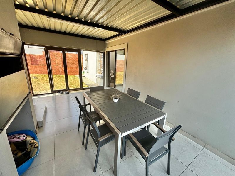 Covered patio area featuring tiled flooring, a built-in braai, and sliding glass doors providing access to the rear garden.