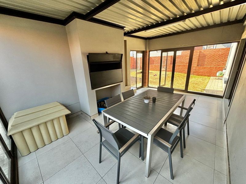 Covered patio area featuring tiled flooring, a built-in braai, and large aluminium sliding doors providing direct access to the rear garden.