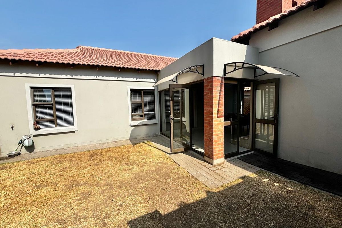 Rear view of the townhouse featuring a paved patio area, brick pillar, and access through glass doors into the living space.