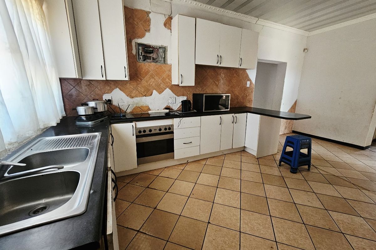 A kitchen featuring built-in cabinetry, a double basin sink, and an integrated oven, currently requiring significant wall repairs and cosmetic updates.
