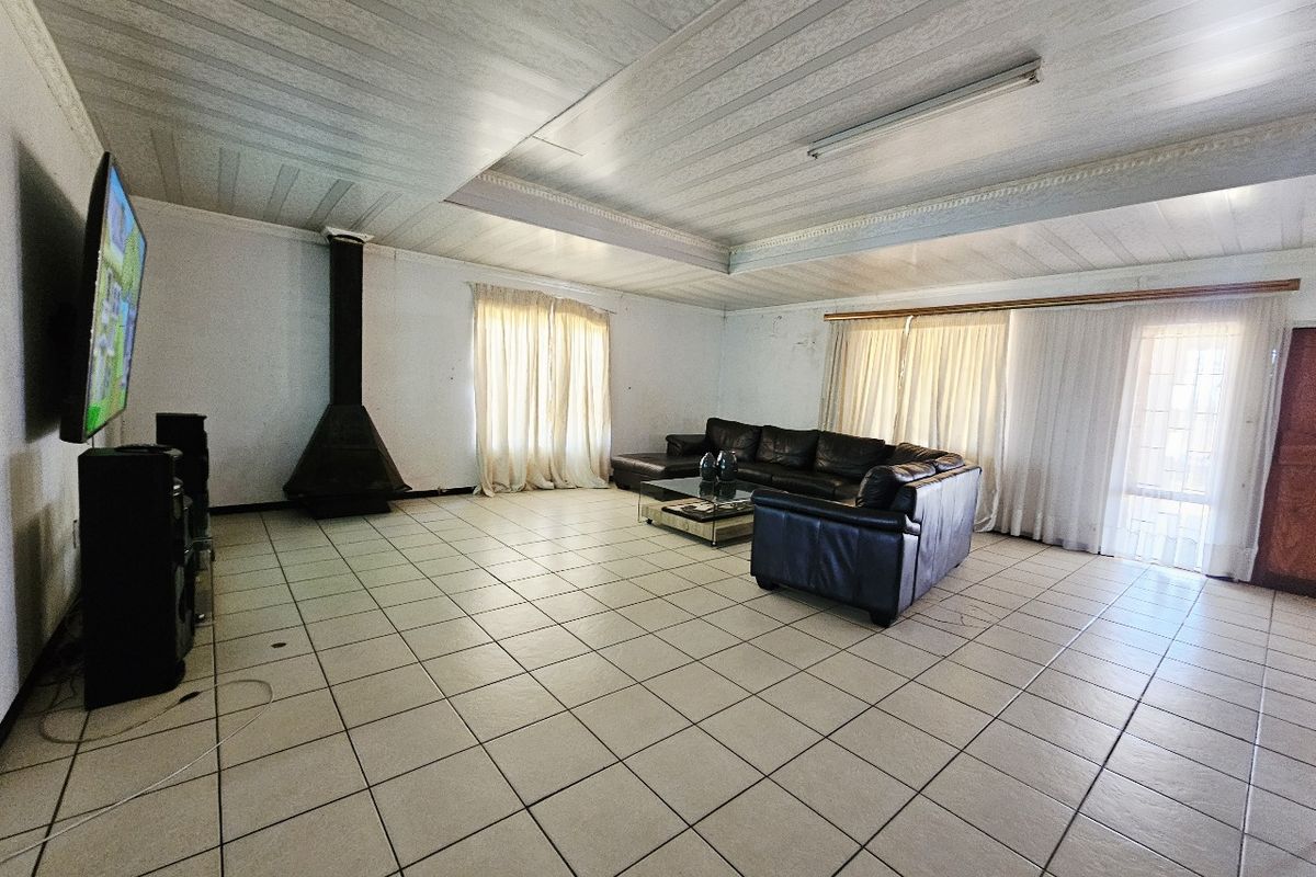 Spacious living room featuring tiled flooring, a freestanding fireplace, and a coffered ceiling, with direct access to the exterior through sliding glass doors.