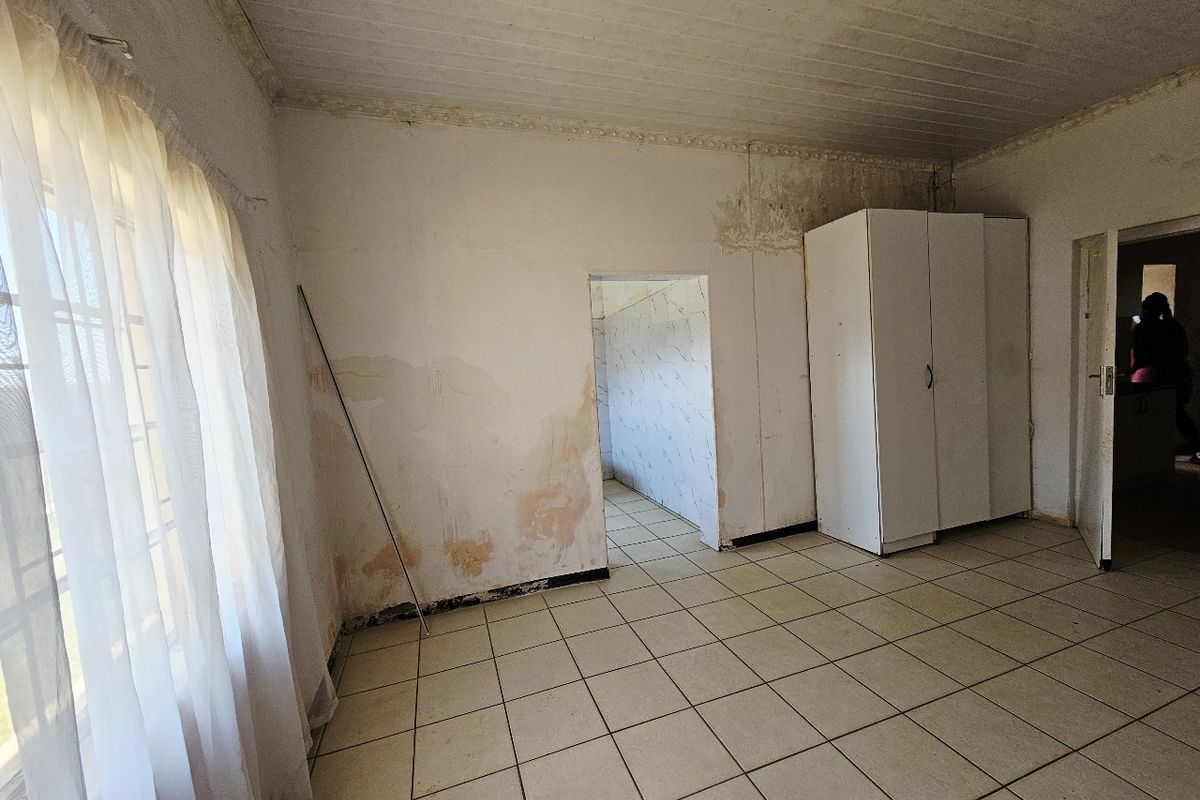 A bedroom featuring tiled flooring and a built-in cupboard, currently showing significant signs of damp and wall deterioration requiring maintenance.
