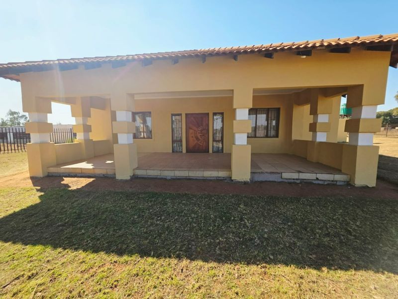 Front elevation of a small holding residence featuring a spacious covered patio, tiled roof, and a decorative wooden entrance door.