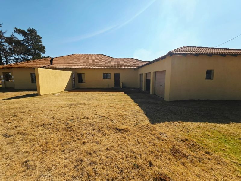 Rear view of the property featuring a large yard, plastered exterior walls, terracotta roof tiles, and multiple garage access points.
