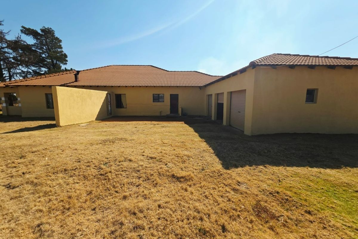 Rear view of the property featuring a large yard, plastered exterior walls, terracotta roof tiles, and multiple garage access points.