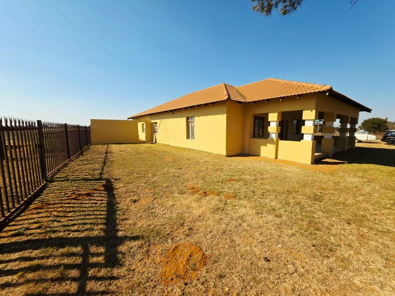Rear view of a single-story small holding residence featuring a terracotta tiled roof, covered patio area, and metal perimeter fencing.