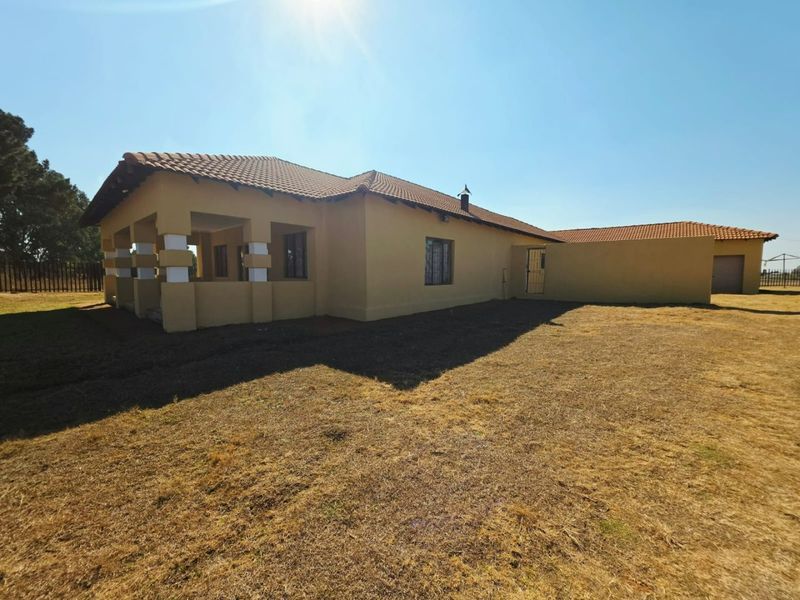 Rear view of the small holding property featuring a covered patio, tiled roof, and attached garage structure set on a large open plot.