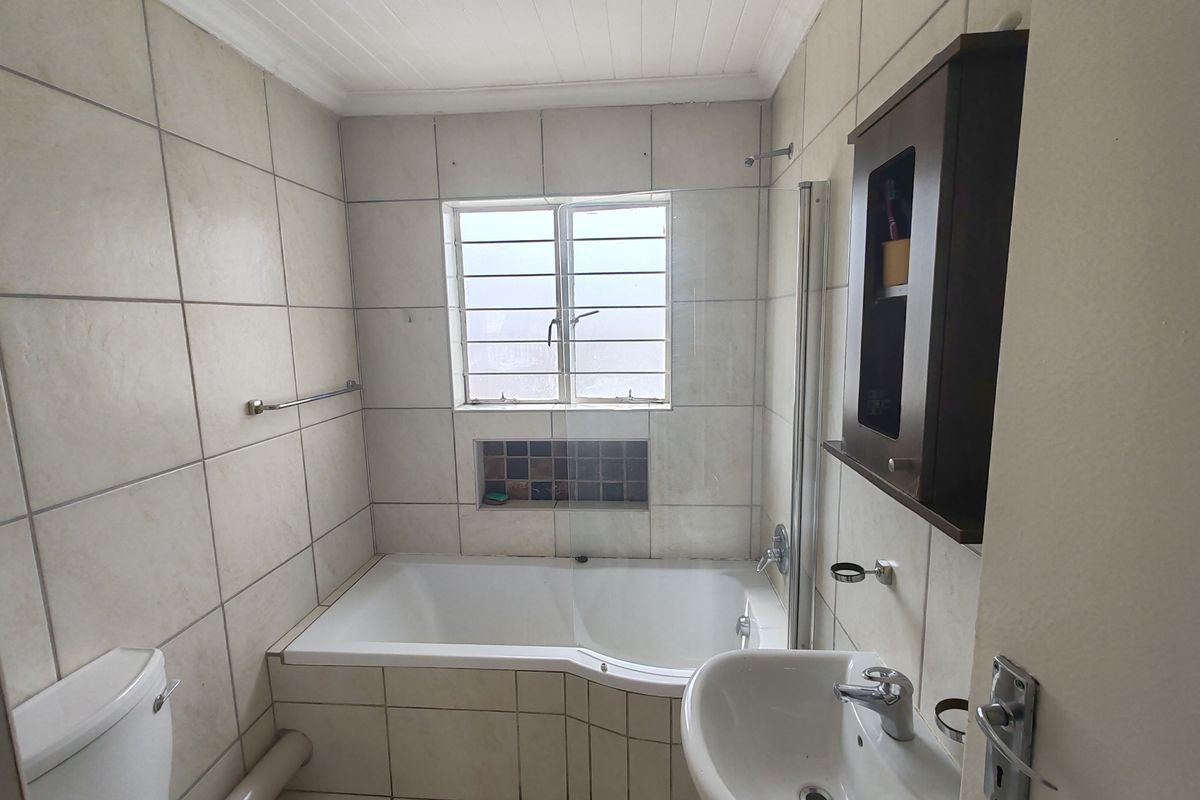 A functional bathroom featuring a built-in bathtub, wall-mounted basin, toilet, and tiled finishes throughout, offering a practical layout for daily use.