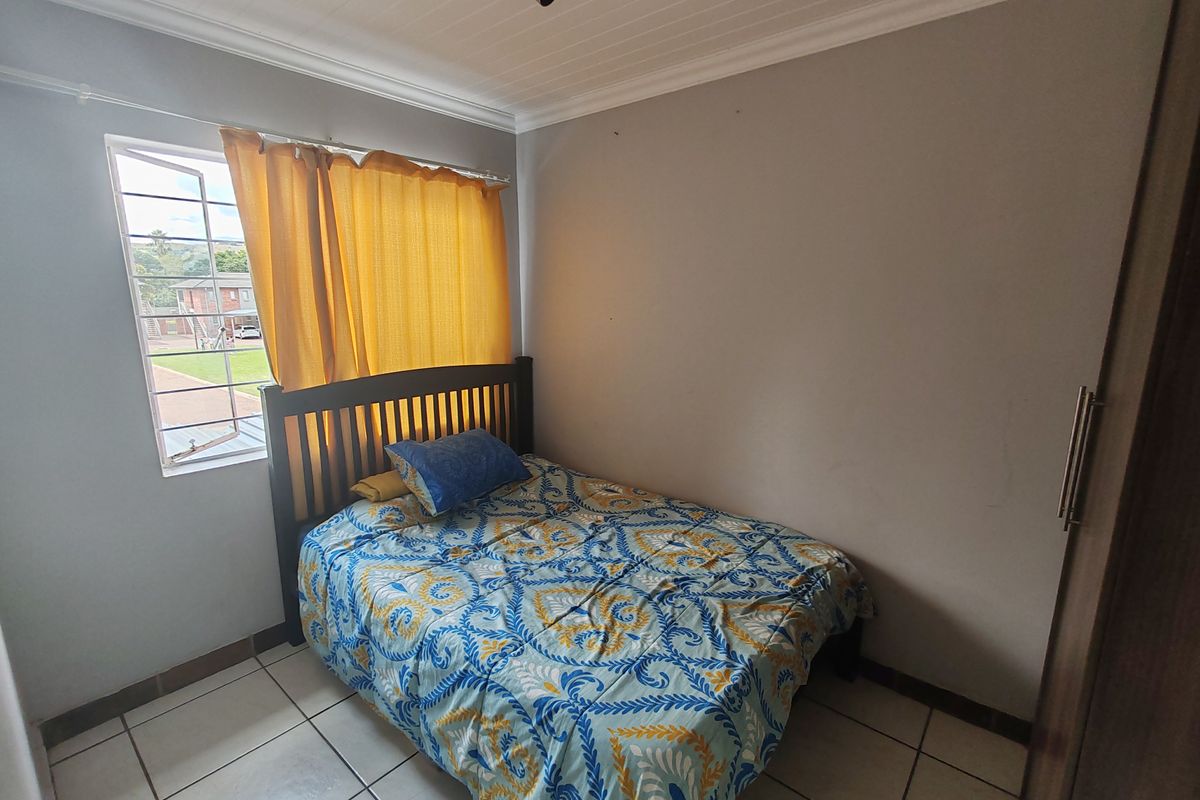 A functional bedroom featuring tiled flooring, a built-in wardrobe, and a window with security bars, providing a simple and practical living space.