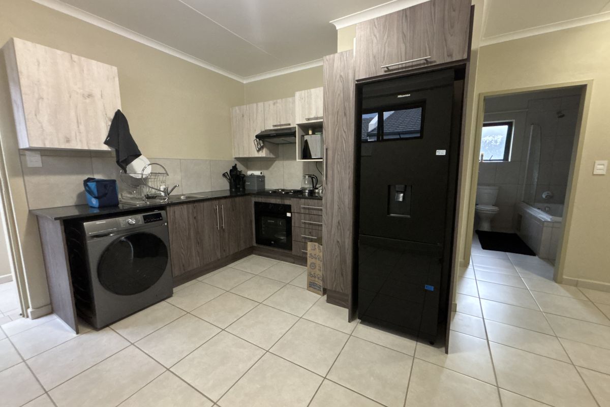 Modern kitchen featuring wood-look cabinetry, dark countertops, built-in oven, gas hob, and tiled flooring, with an adjacent bathroom visible.
