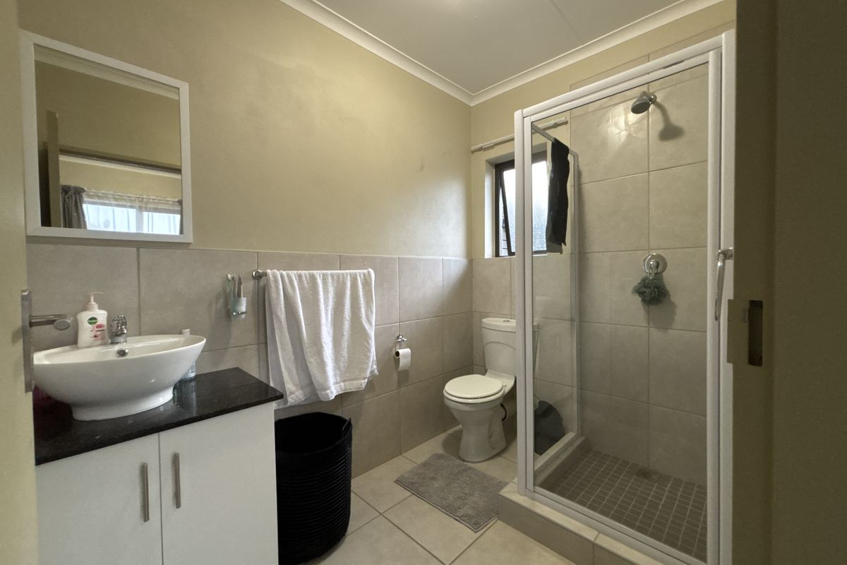 A functional bathroom featuring a vanity with a vessel sink, a glass-enclosed shower, and neutral wall and floor tiling.