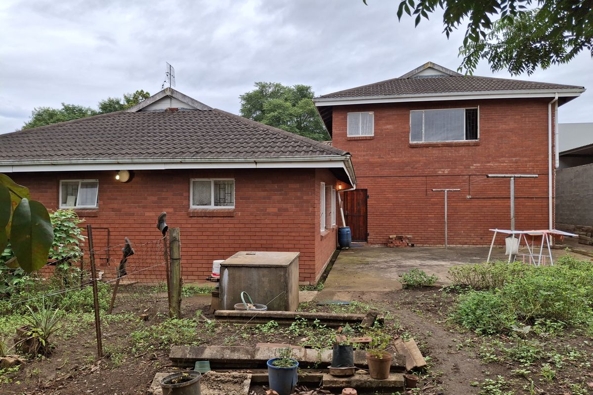 Rear view of a double-story red brick house featuring a concrete patio area and an established garden space.