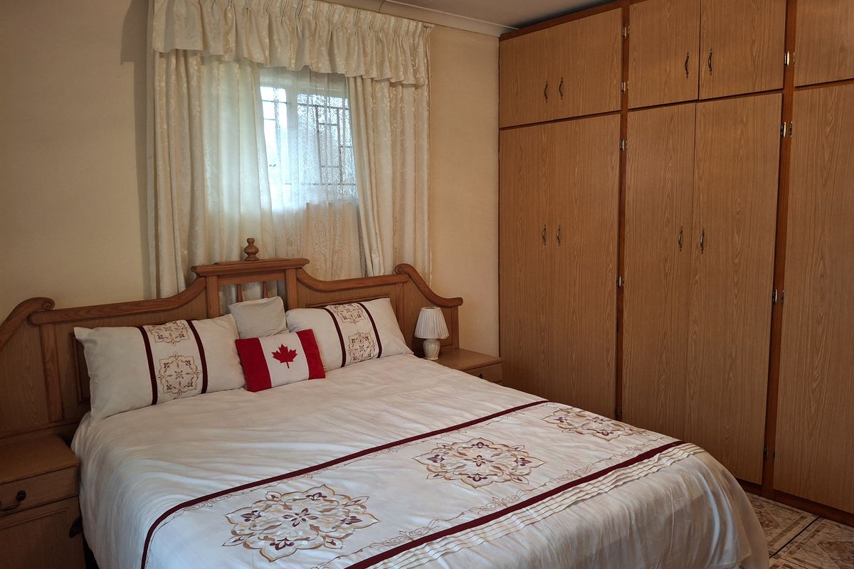 A bedroom featuring built-in wooden cupboards and a window with security bars, providing functional storage and natural light.