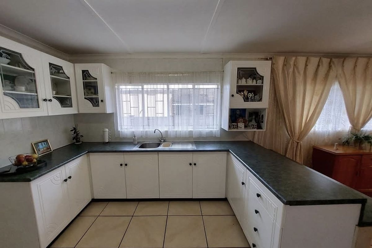 A functional U-shaped kitchen featuring white cabinetry, dark laminate countertops, a stainless steel sink, and tiled flooring.