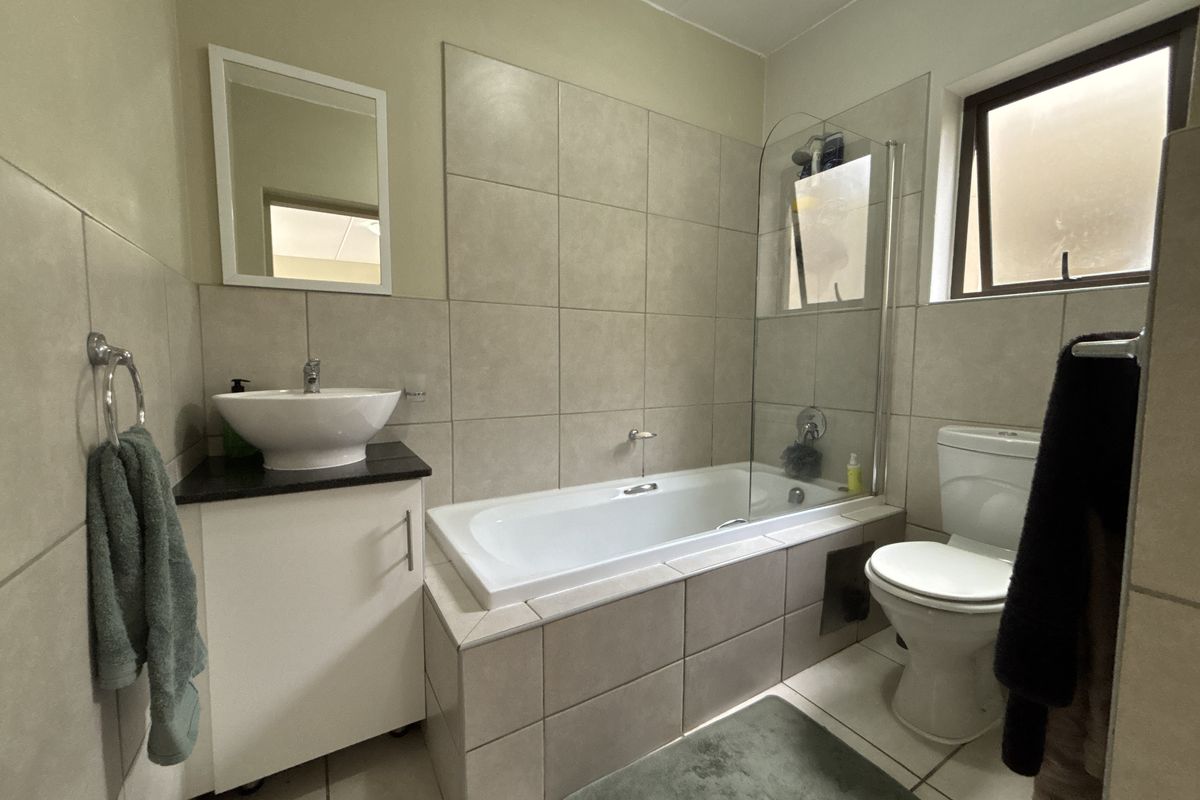 A functional bathroom featuring a vessel sink vanity, a bathtub with a glass shower screen, and neutral wall and floor tiling.