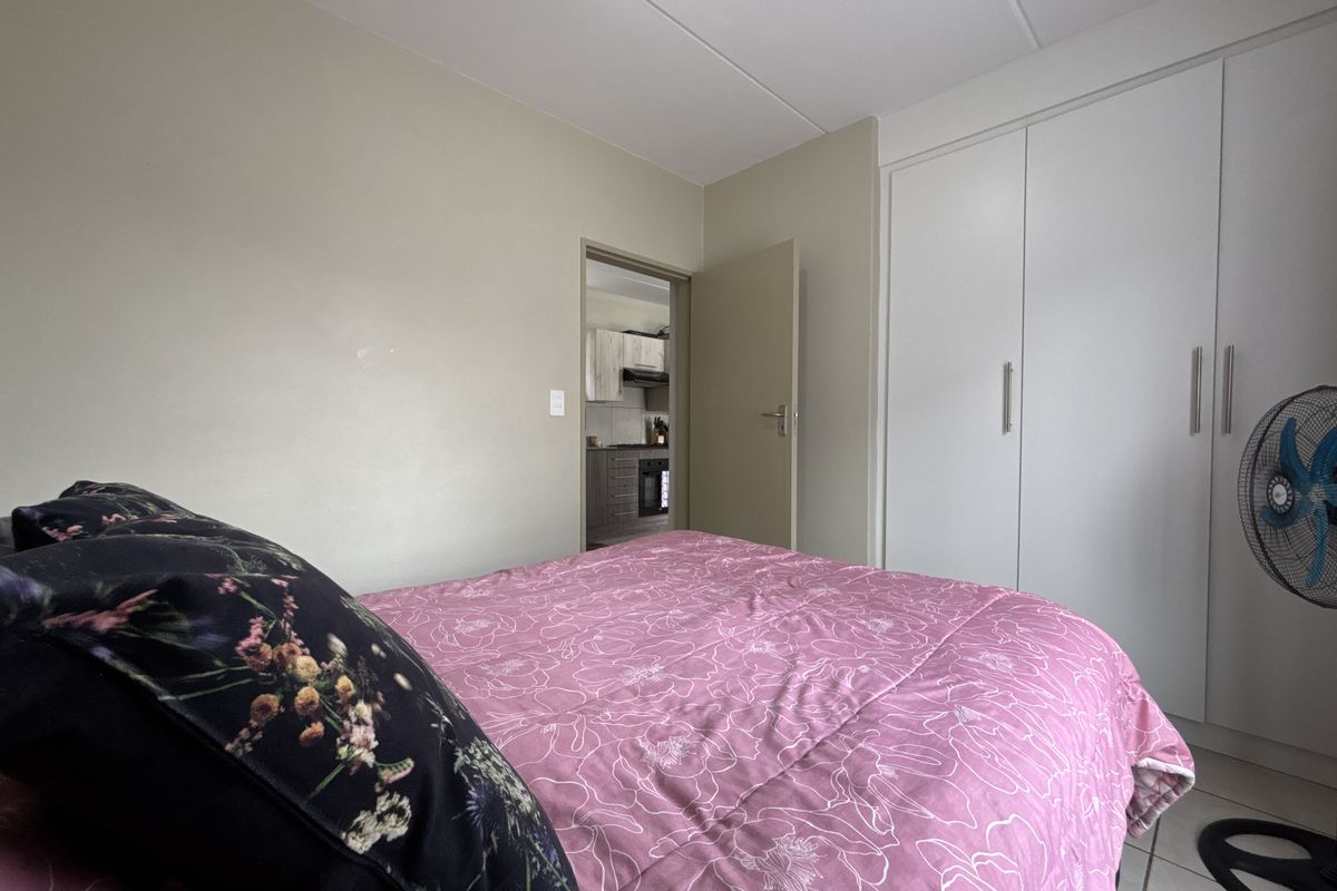 A bedroom featuring built-in cupboards and tiled flooring, with a view through the doorway into the kitchen area.