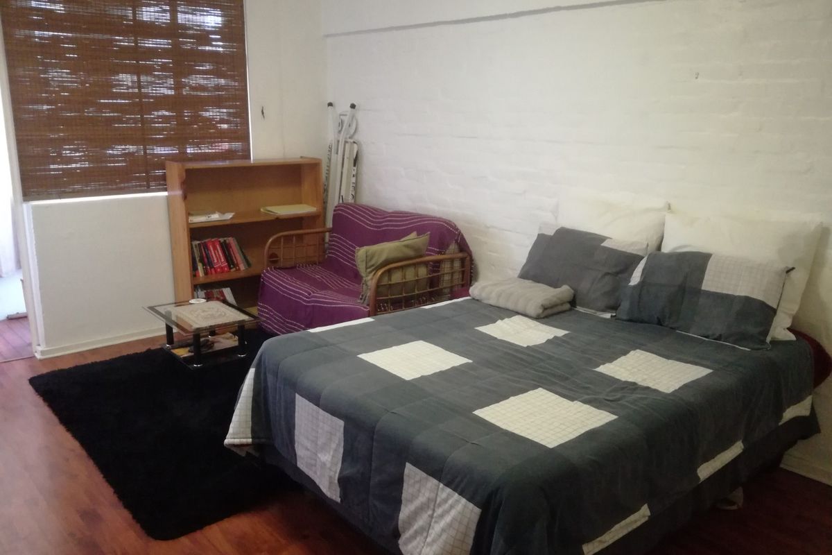 A bedroom featuring laminate flooring, a painted brick feature wall, and a bamboo roller blind.
