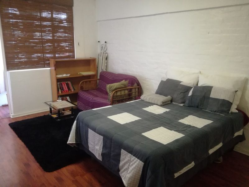 A bedroom featuring laminate flooring, a painted brick feature wall, and a bamboo roller blind.
