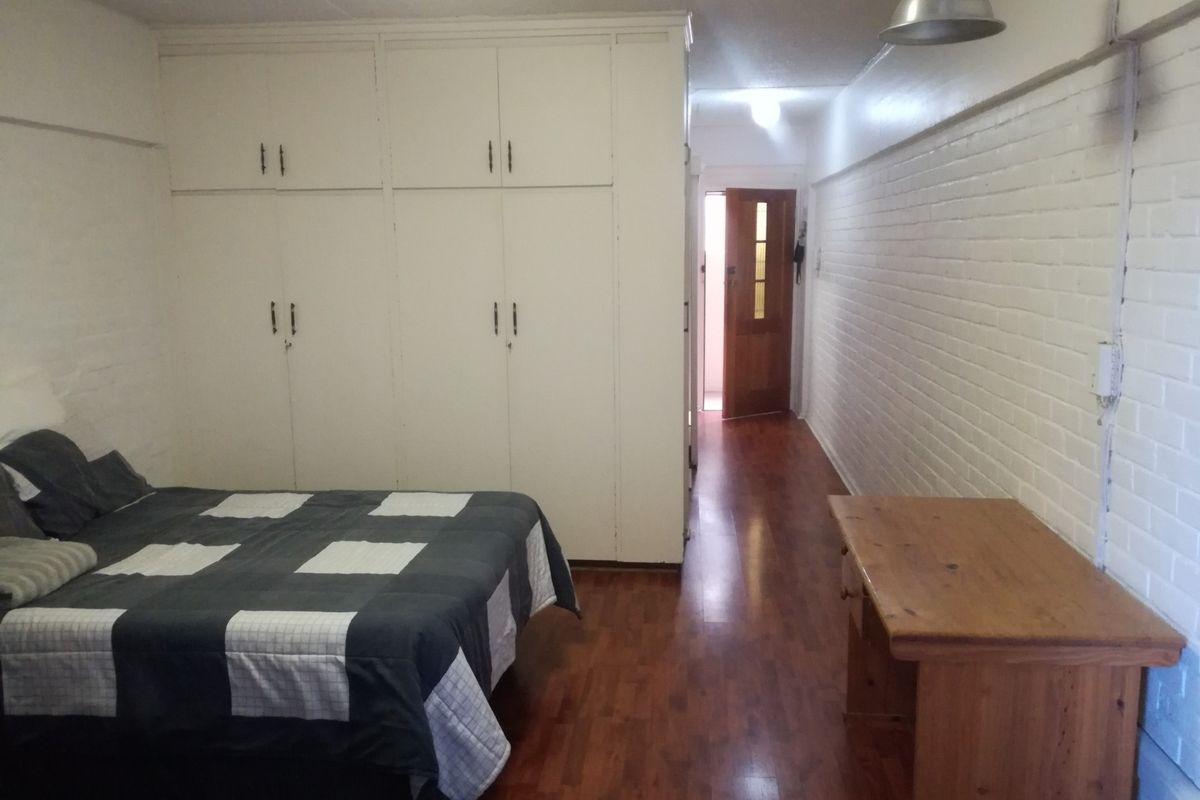 Bedroom featuring built-in cupboards, laminate flooring, and a painted brick wall, providing a functional space with direct access to the hallway.