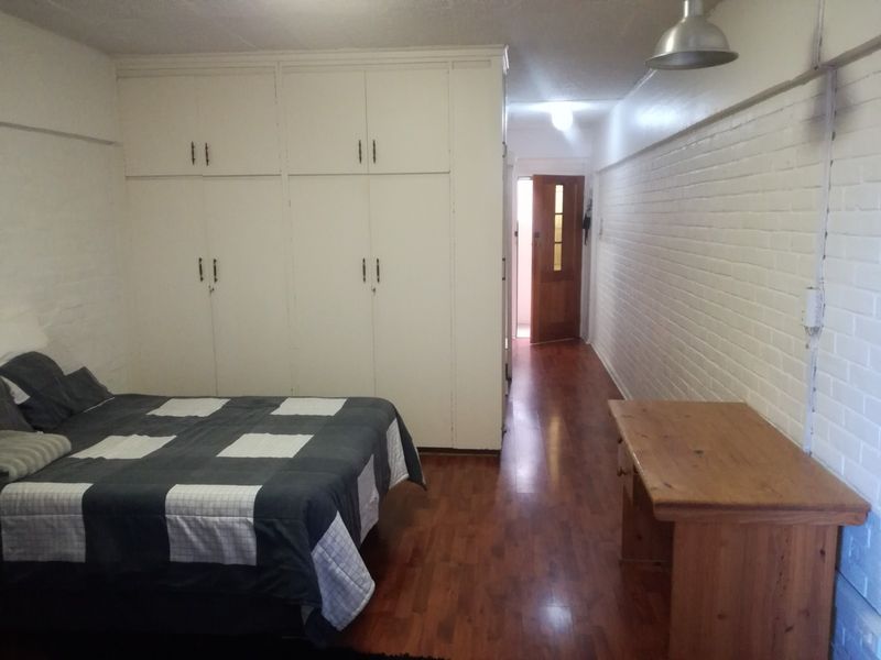 Bedroom featuring built-in cupboards, laminate flooring, and a painted brick wall, providing a functional space with direct access to the hallway.
