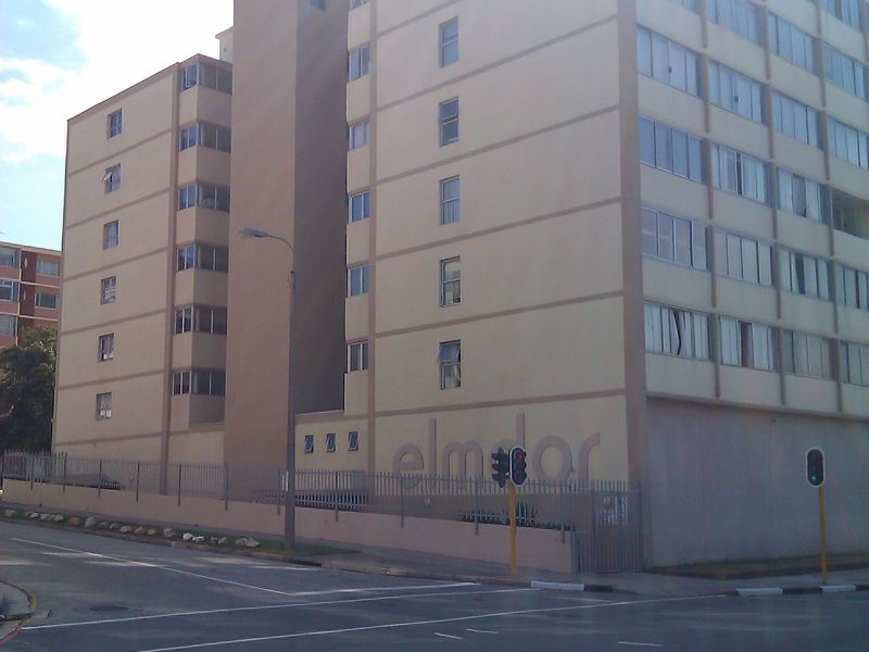 Exterior view of a multi-story apartment building featuring a beige facade and perimeter fencing, situated on a street corner.