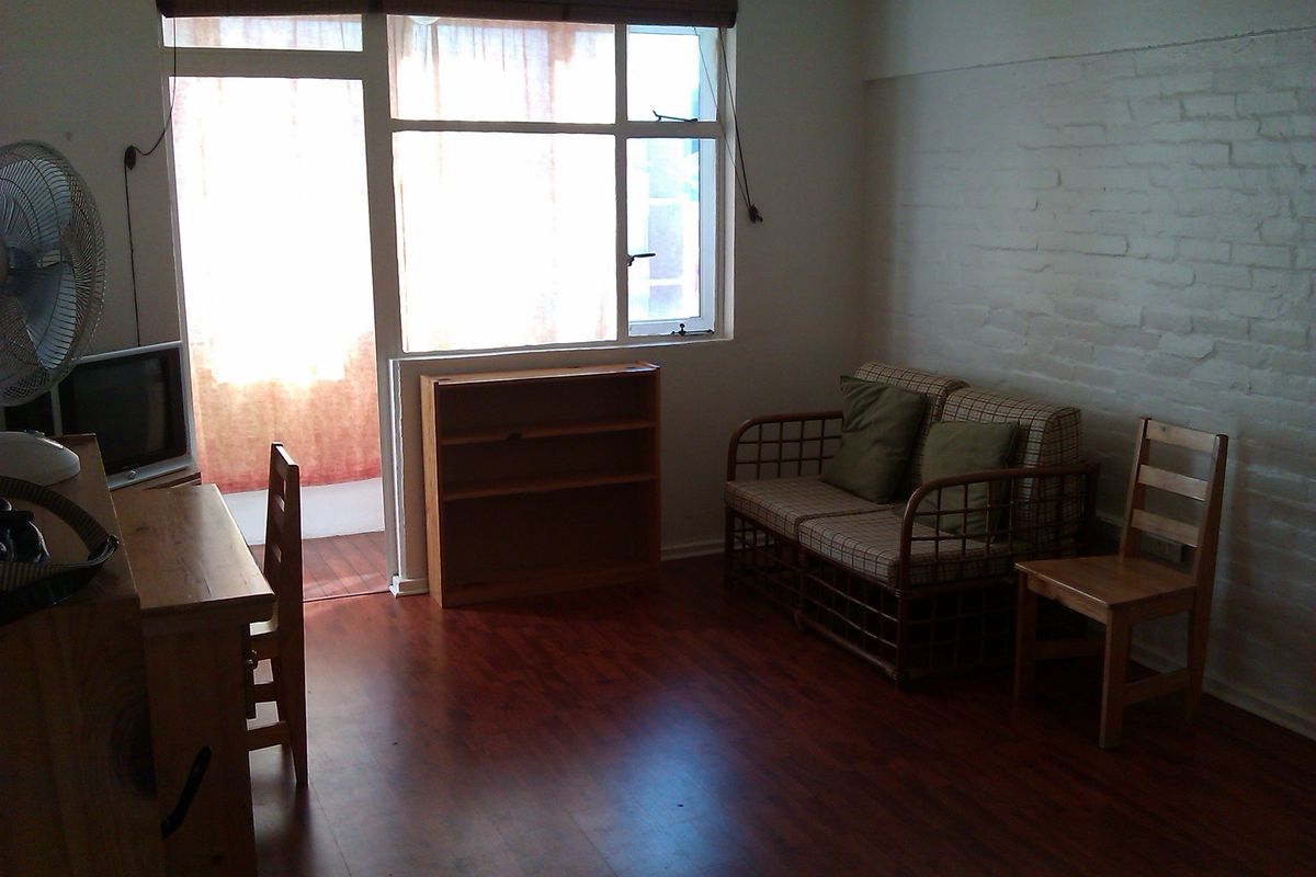 A living room featuring laminate flooring, an exposed brick wall, and large windows providing natural light and access to an outdoor area.