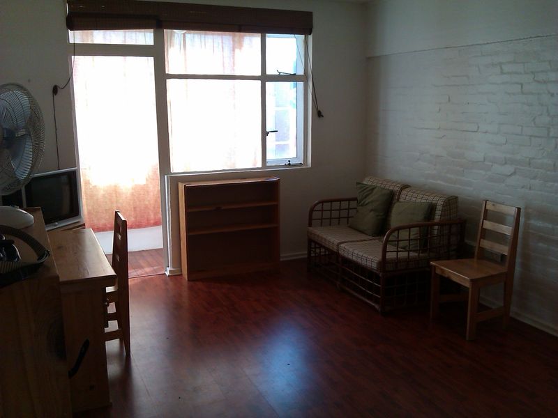 A living room featuring laminate flooring, an exposed brick wall, and large windows providing natural light and access to an outdoor area.
