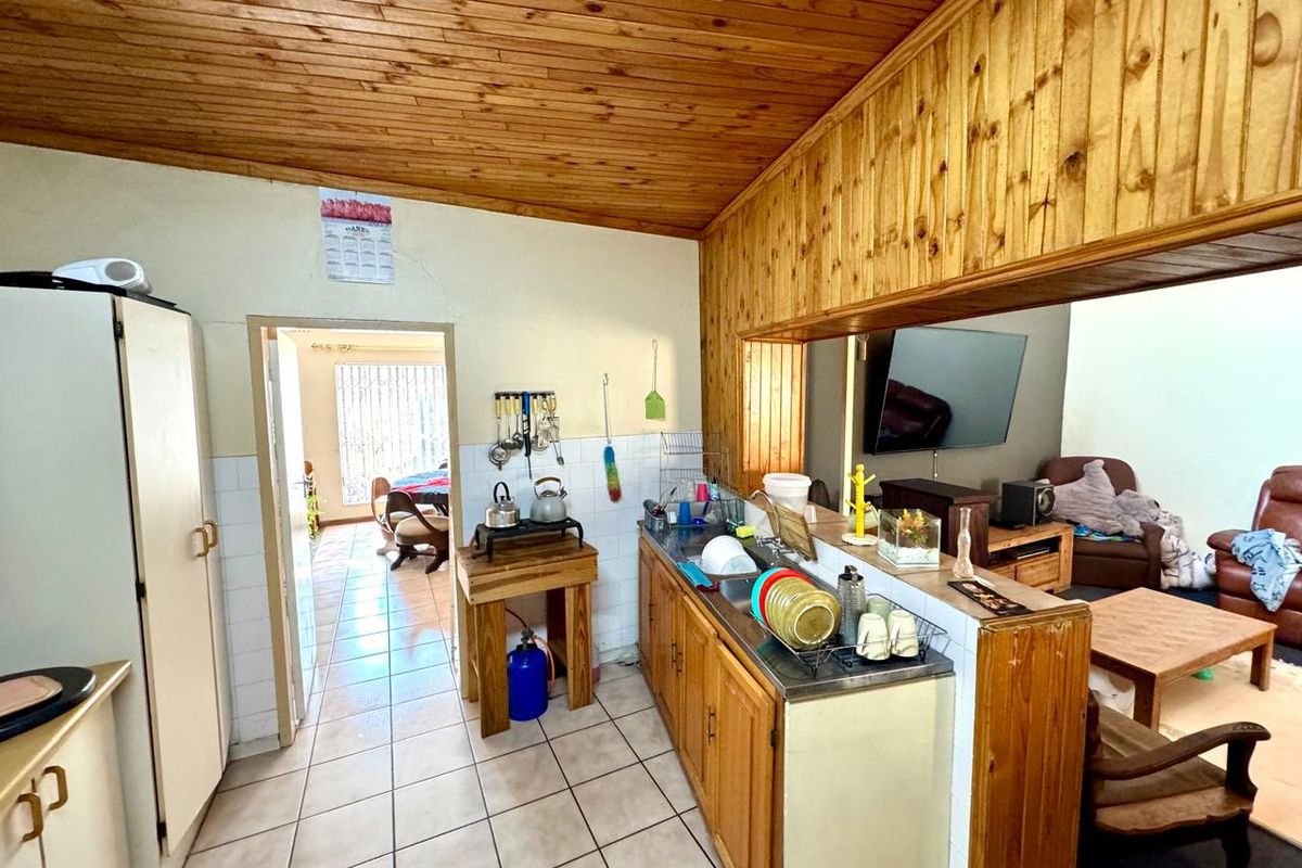 A dated kitchen area featuring wooden cabinetry, tiled flooring, and a timber-clad ceiling, opening into an adjacent living space.