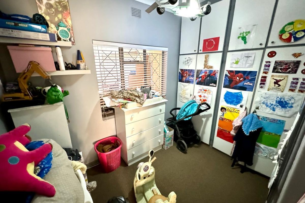 A bedroom featuring built-in floor-to-ceiling storage cupboards and a window with security bars.