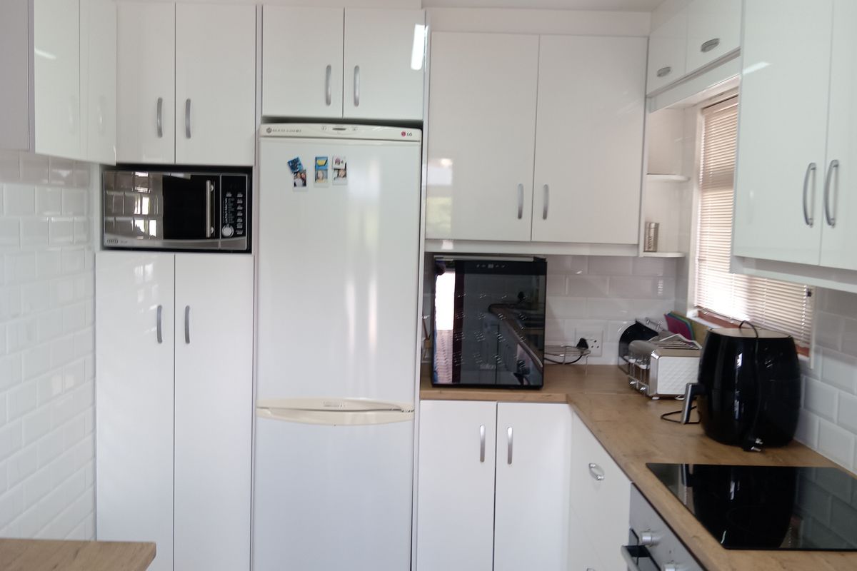 A modern kitchen featuring white cabinetry, wood-look countertops, a built-in oven, and a glass hob, complemented by a classic subway tile backsplash.