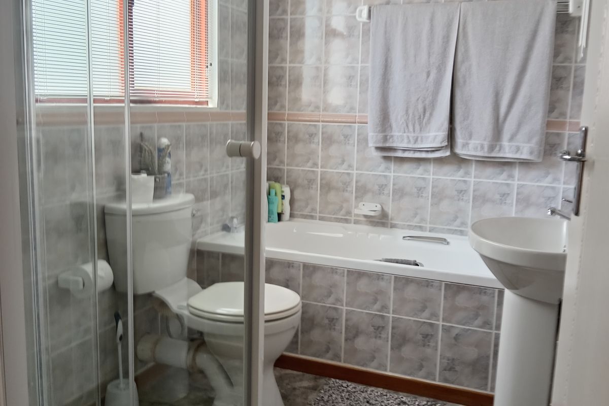 A functional bathroom featuring a pedestal basin, a built-in bathtub, and a separate glass-enclosed shower cubicle with tiled walls.