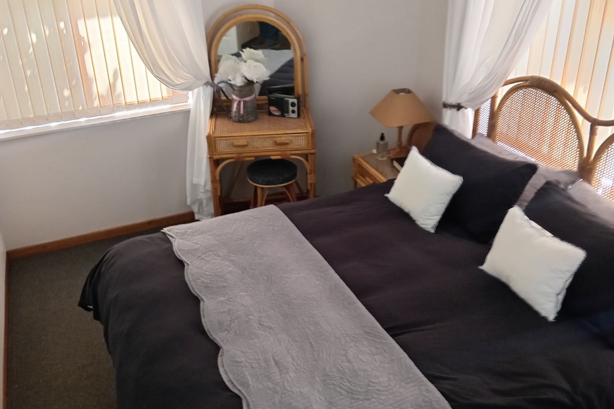 A well-lit bedroom featuring dual aspect windows with vertical blinds, neutral wall finishes, and carpeted flooring.